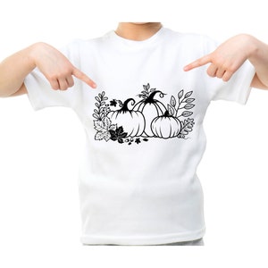 May include: A white t-shirt with a black and white illustration of three pumpkins with leaves and stems.