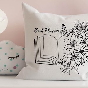 May include: A white pillow with black line art of an open book with flowers and a butterfly. The text "Book Flowers" is printed on the pillow.