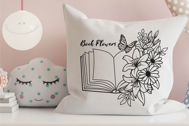 May include: A white pillow with black line art of an open book with flowers and a butterfly. The text "Book Flowers" is printed on the pillow.
