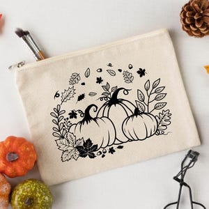 May include: A white canvas makeup bag with a black and white design of pumpkins and fall leaves.