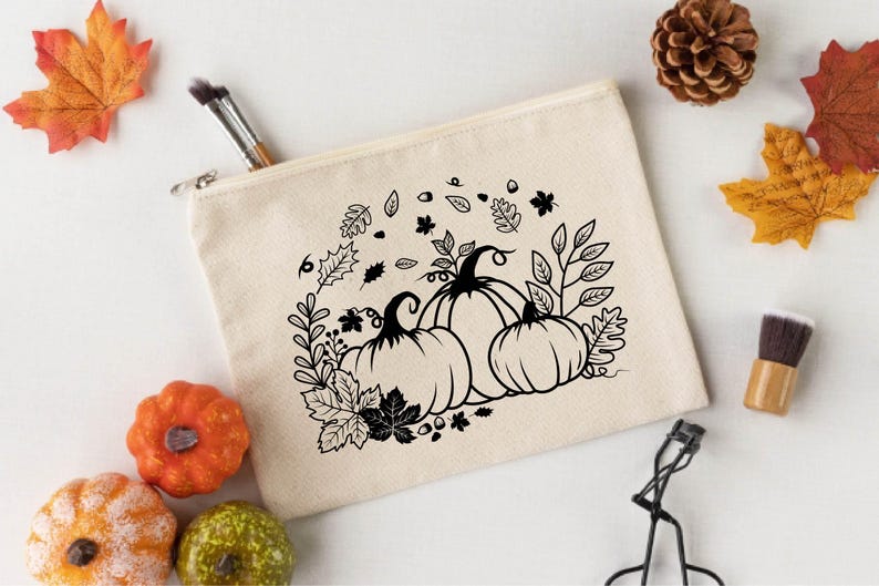May include: A white canvas makeup bag with a black and white design of pumpkins and fall leaves.