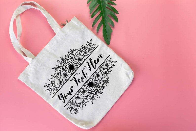 K&ouml;nnte beinhalten: Wei&szlig;e Canvas-Tragetasche mit schwarzem Blumendesign und dem Text "Your Text Here" auf der Vorderseite.