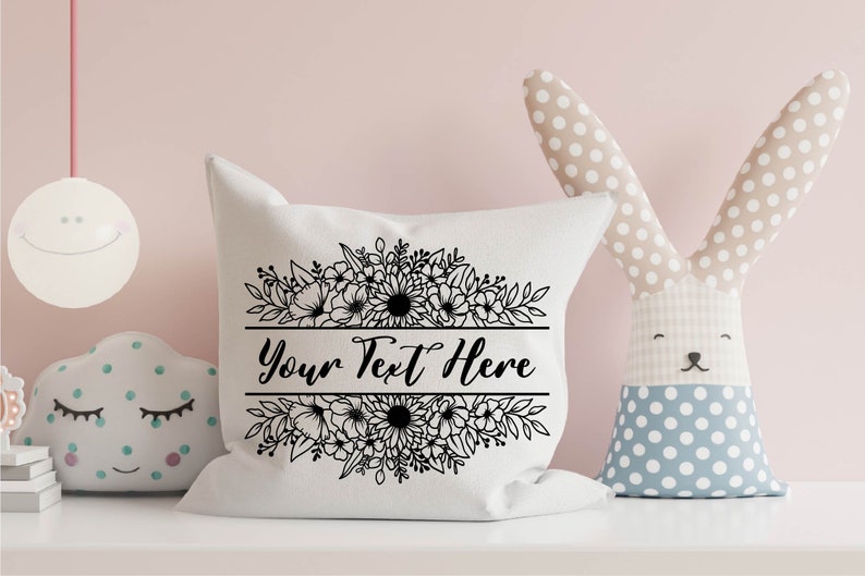 K&ouml;nnte beinhalten: Ein wei&szlig;es Kissen mit einem schwarzen Blumendesign und dem Text "Your Text Here" in einer dekorativen Schrift.