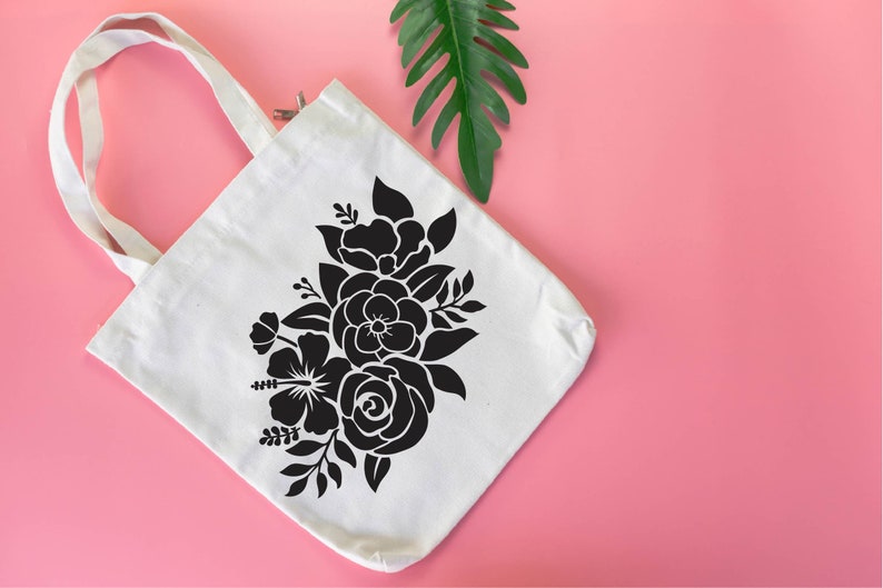 Pode incluir: Uma bolsa tote de lona branca com um design floral preto. A bolsa tem um fecho de correr e duas al&ccedil;as.
