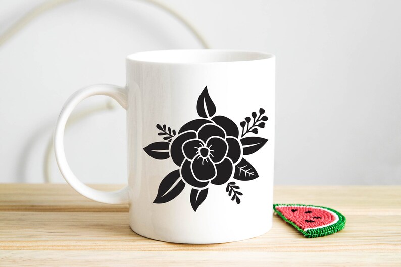 Pode incluir: Caneca de cer&acirc;mica branca com uma silhueta preta de uma flor com folhas. A flor tem cinco p&eacute;talas e um centro.