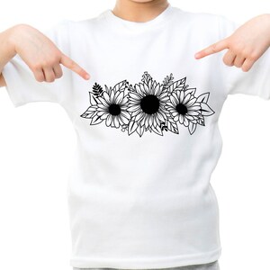 May include: White t-shirt with a black and white floral design of three sunflowers and leaves. The graphic is centered on the shirt. The shirt is being pointed at by two hands.