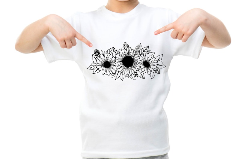 May include: White t-shirt with a black and white floral design of three sunflowers and leaves. The graphic is centered on the shirt. The shirt is being pointed at by two hands.