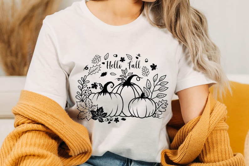 May include: White t-shirt with a black and white graphic design of pumpkins and leaves. The text "Hello Fall" is written on the shirt.