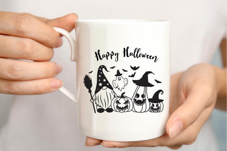 May include: White ceramic mug with a black and white design featuring a gnome, a ghost, and pumpkins. The text "Happy Halloween" is printed on the mug.