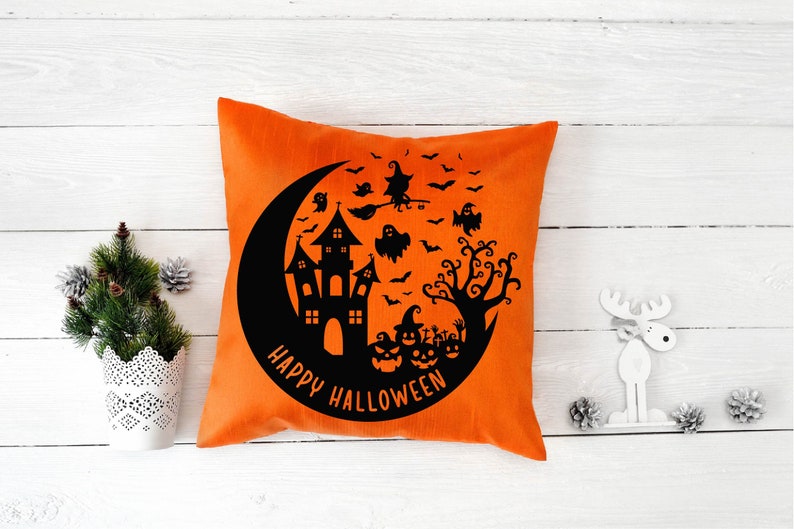 May include: Orange throw pillow with a black silhouette of a haunted house, a crescent moon, bats, ghosts, a witch flying on a broomstick, and a tree. The text "Happy Halloween" is written in a circle around the design.