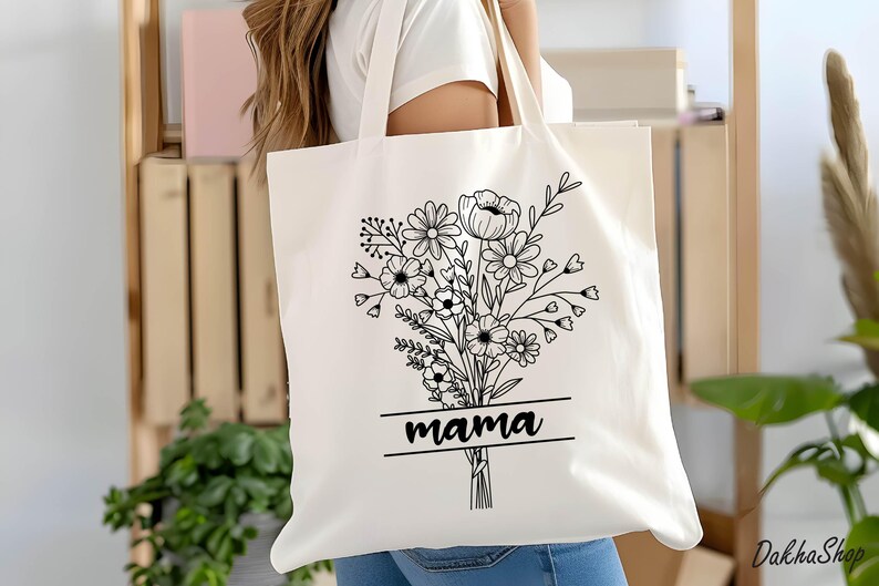 May include: Cream-colored tote bag featuring a black floral bouquet design with the word "mama" in a rectangular frame. The bag has long handles and is made of a sturdy fabric, suitable for carrying various items. The design is simple and elegant.