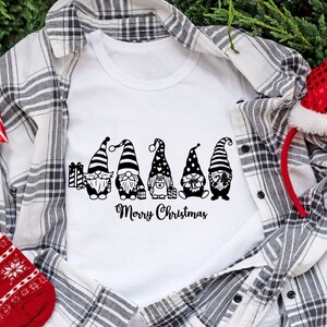 May include: White t-shirt with a black and white graphic of five gnomes holding gifts and the text "Merry Christmas".