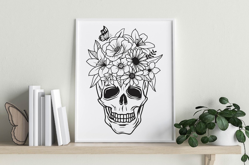 May include: Black and white line art print of a skull with a floral crown. The skull has a detailed design with a flower crown on top. The print is on a white background.
