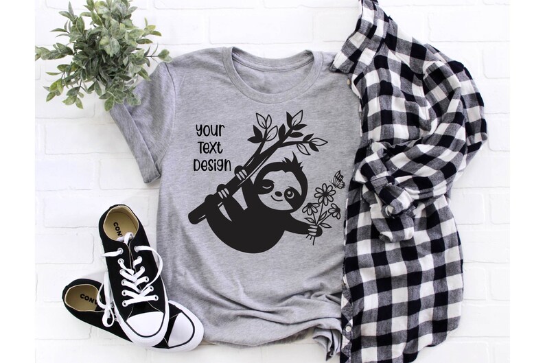 May include: Gray t-shirt with a black sloth design holding flowers and hanging from a branch. The text "Your Text Design" is printed on the shirt.