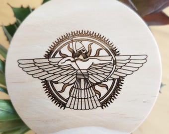 Puede incluir: Un posavasos de madera con un diseño grabado con láser de una figura alada que sostiene un arco y una flecha, rodeado de un sol radiante.
