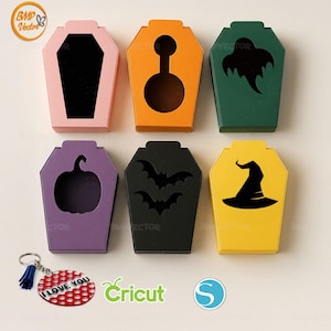 May include: Six colourful coffin-shaped boxes with cut-out designs, including a pumpkin, bats, and a witch's hat. A keychain with "I Love You" text and a red and white pattern is also present. The boxes are in pink, orange, green, purple, black, and yellow.