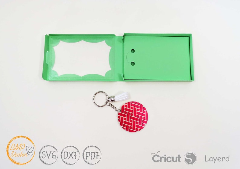 May include: A green card with a white scalloped border and a white tassel keychain with a red and white patterned circle charm.