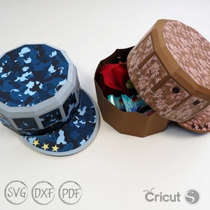May include: Two papercraft boxes shaped like military caps. One is blue camouflage with three gold stars on the brim. The other is pink camouflage with three brown stars on the brim.