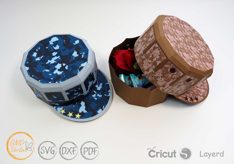 May include: Two papercraft boxes shaped like military caps. One is blue camouflage with three gold stars on the brim. The other is pink camouflage with three brown stars on the brim.