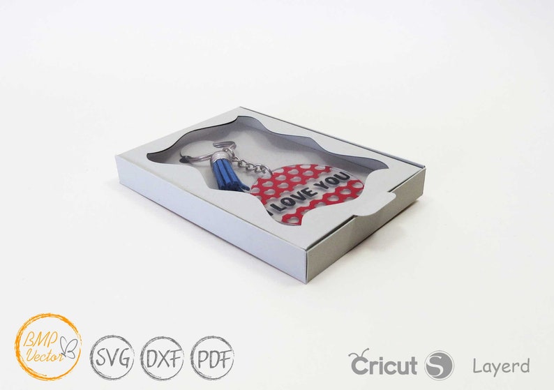 May include: A red heart-shaped keychain with white polka dots and the text "I LOVE YOU" in black. The keychain is attached to a silver key ring with a blue tassel. The keychain is displayed in a white box with a clear window.