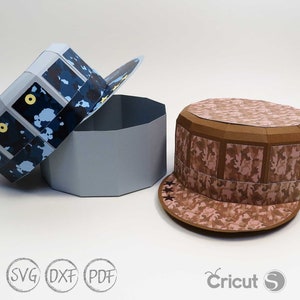 May include: Two papercraft hats, one blue and one brown, with camouflage patterns. The blue hat is open and the brown hat is closed. Both hats have a star design on the brim. The hats are made of paper and are designed to be assembled.