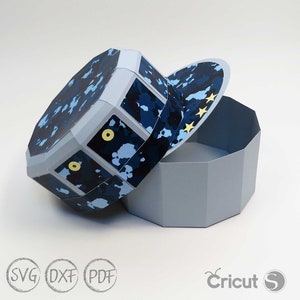 May include: A blue and white camouflage patterned paper box with a lid shaped like a baseball cap. The lid has yellow stars on it. The box is open and the lid is laying next to it.