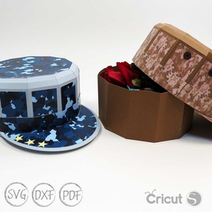 May include: Two papercraft boxes shaped like military hats. The box on the left is blue with a camouflage pattern and stars. The box on the right is brown with a camouflage pattern. Both boxes are open and have a brown interior.