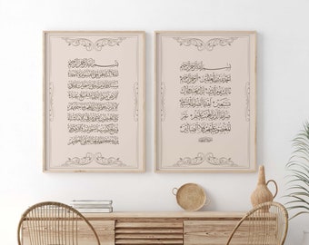 May include: Two framed prints with Arabic calligraphy in black ink on a light pink background. The prints are hanging on a white wall above a wooden cabinet with two wicker chairs and a small wicker table. A potted plant is on the right side of the image.