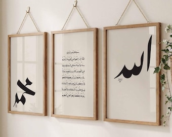 May include: Three framed art prints with Arabic calligraphy. Each print has a wooden frame and is suspended by a gold chain. The prints feature black calligraphy on a cream background. The frames are hanging on a white wall.