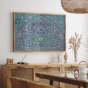 Puede incluir: Una impresión enmarcada de un intrincado diseño floral azul y verde con un arco decorativo. La impresión está colgada en una pared blanca sobre un armario de madera con puertas de ratán tejido.