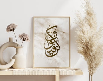 May include: A framed print with a gold Arabic calligraphy design on a white marble background. The text reads "Be and it is".