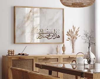 May include: A framed mirror with a white marble-like background and a gold Arabic calligraphy inscription that reads "Masha Allah" hanging on a white wall above a wooden cabinet with woven rattan doors.