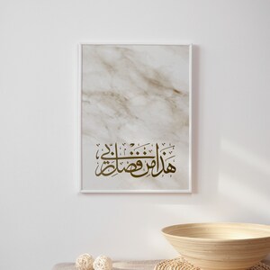 May include: A framed print with a marble background and gold Arabic calligraphy that reads "Masha Allah" in a white frame on a white wall. A wooden bowl and two woven balls are on a beige linen tablecloth.