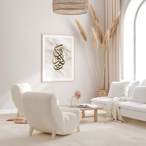 May include: A living room interior with a white couch, two white fluffy armchairs, a coffee table, a vase with pink flowers, and a framed print with Arabic calligraphy and the text "Be and Stay".