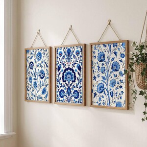 以下が含まれることがあります： 青と白の花柄の3つの額入りウォールアート。アートワークは長方形で、木製のフレームと吊り下げ用のチェーンが付いています。花柄は複雑なディテールとクラシックな美学が特徴です。