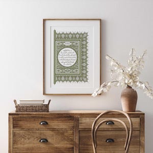 May include: A framed print of an Islamic calligraphy design in green and white. The design features intricate patterns and a circular frame with Arabic text.
