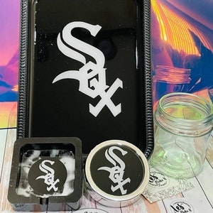 May include: A black rolling tray, ashtray, grinder, and jar set. Each item features the white "Sox" logo. The set includes stickers that say "les make it". The tray is rectangular with a decorative border.