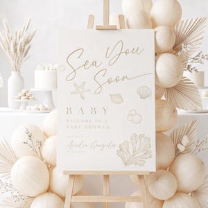 Puede incluir: Un letrero rectangular blanco sobre un caballete de madera con el texto Sea You Soon, BABY, WELCOME TO A BABY SHOWER y Amelia Gonzalez. El letrero está decorado con dibujos lineales dorados de una estrella de mar, conchas y coral, rodeado de globos beige.