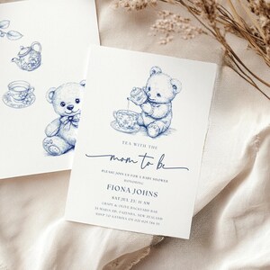Puede incluir: Invitación de baby shower azul y blanca con un osito de peluche sosteniendo una tetera y una taza de té. La invitación dice "Té con la futura mamá" e incluye la fecha, la hora y el lugar del evento.