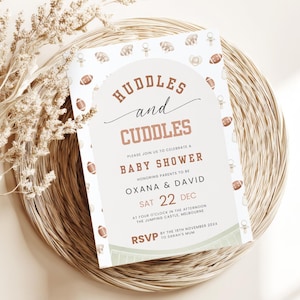 Könnte beinhalten: Eine Babyparty-Einladung mit dem Text "Huddles and Cuddles" in Braun und Weiß. Die Einladung enthält Details für die Babyparty von Oxana & David am 22. Dezember. Die Einladung ist mit Baby-Illustrationen verziert und liegt auf einer gewebten Matte.