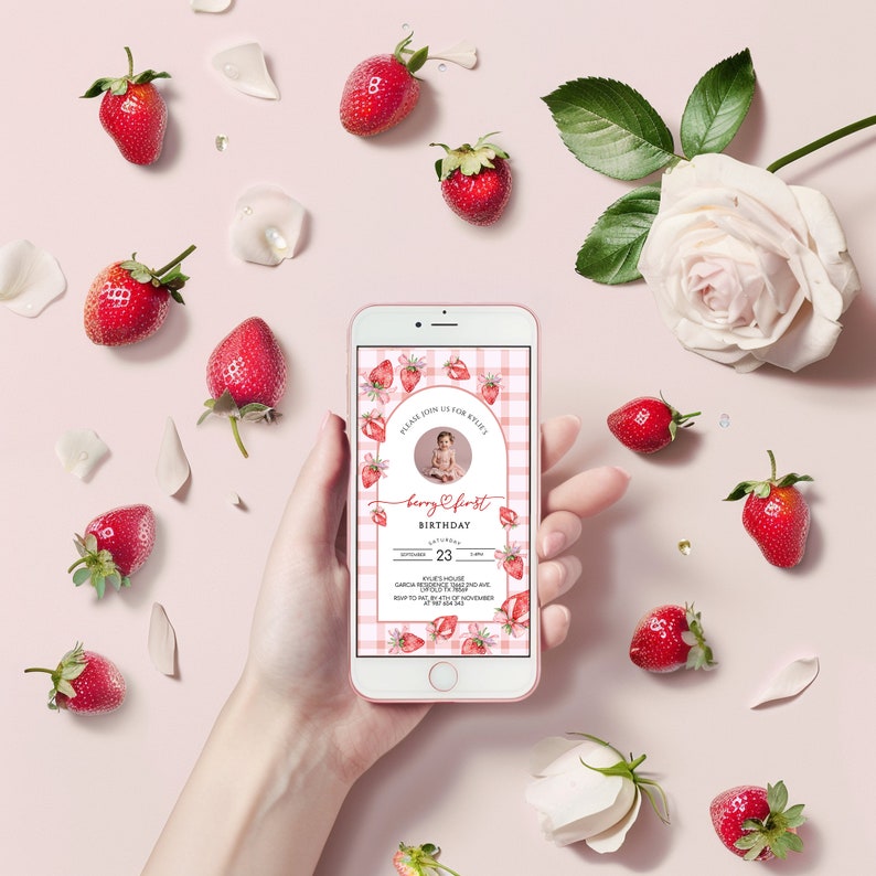 May include: A pink and white gingham background with a strawberry design. The text reads "Please join us for Kylie's Berry First Birthday". The date is November 23rd. The invitation is on a mobile phone.