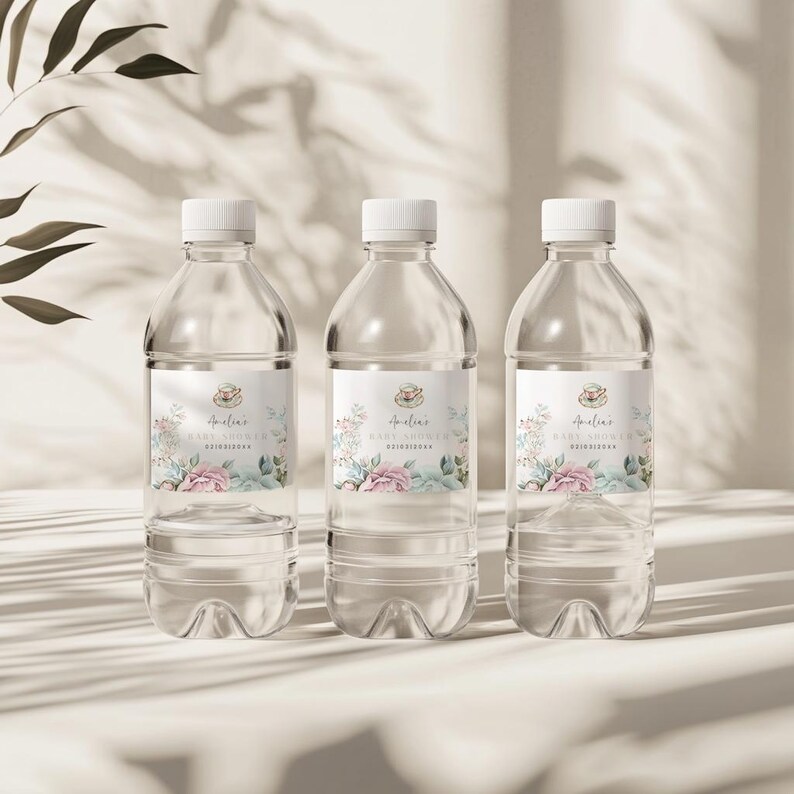 K&ouml;nnte beinhalten: Drei durchsichtige Plastikwasserflaschen mit personalisierten Etiketten f&uuml;r eine Babyparty. Die Etiketten zeigen ein Blumenmuster mit rosa und blauen Blumen und den Text "Amelia's Baby Shower".