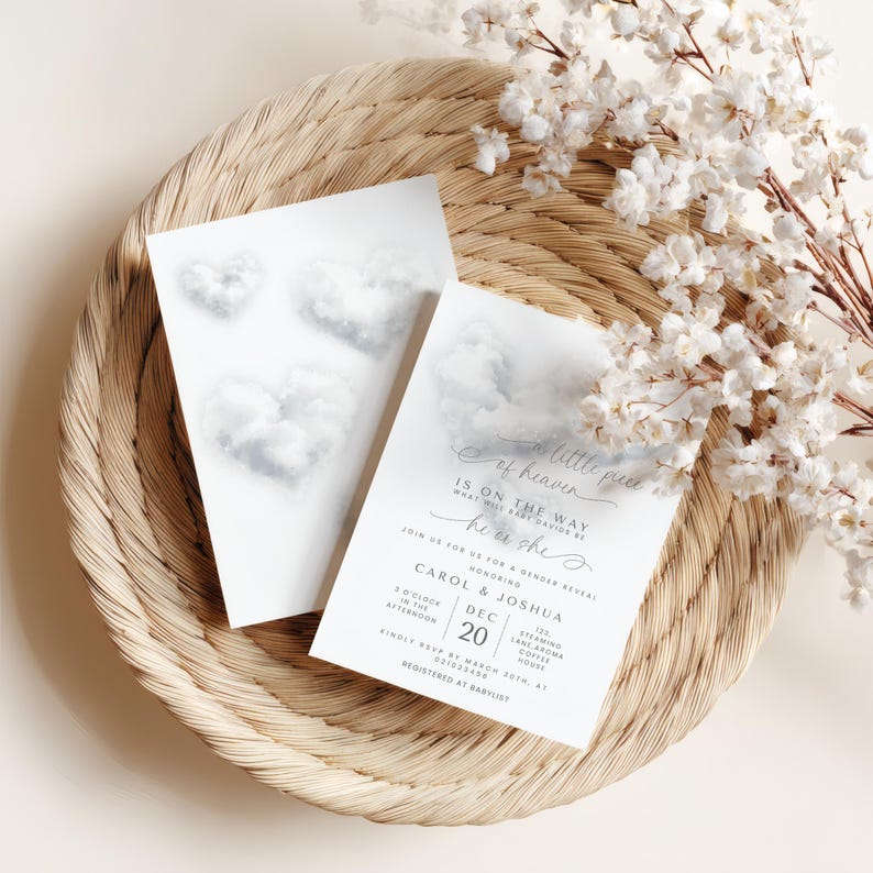 May include: Two white gender reveal invitations with cloud heart designs, resting on a woven tray with white floral accents. The text reads "A little piece of heaven, is on the way, he or she".