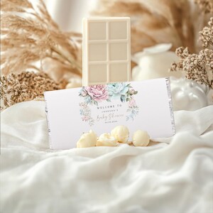 K&ouml;nnte beinhalten: Wei&szlig;e Schokoladentafel in einer wei&szlig;en und silbernen Folienverpackung mit einem Blumendesign und dem Text "Willkommen zur Babyparty von [Name]".