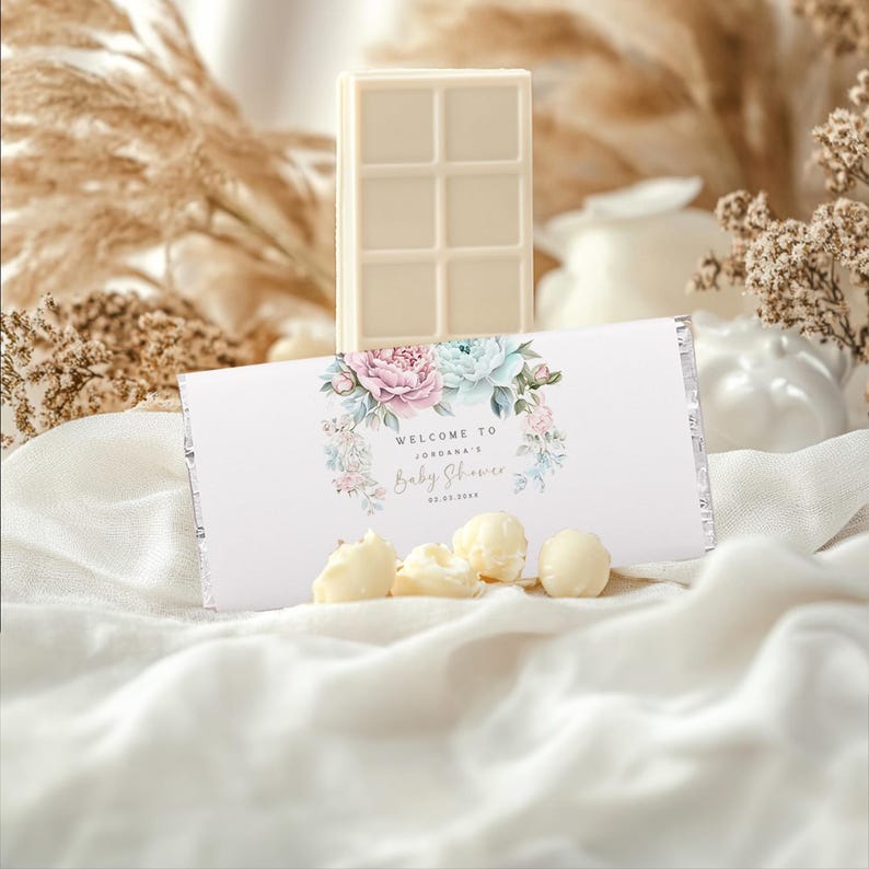 K&ouml;nnte beinhalten: Wei&szlig;e Schokoladentafel in einer wei&szlig;en und silbernen Folienverpackung mit einem Blumendesign und dem Text "Willkommen zur Babyparty von [Name]".