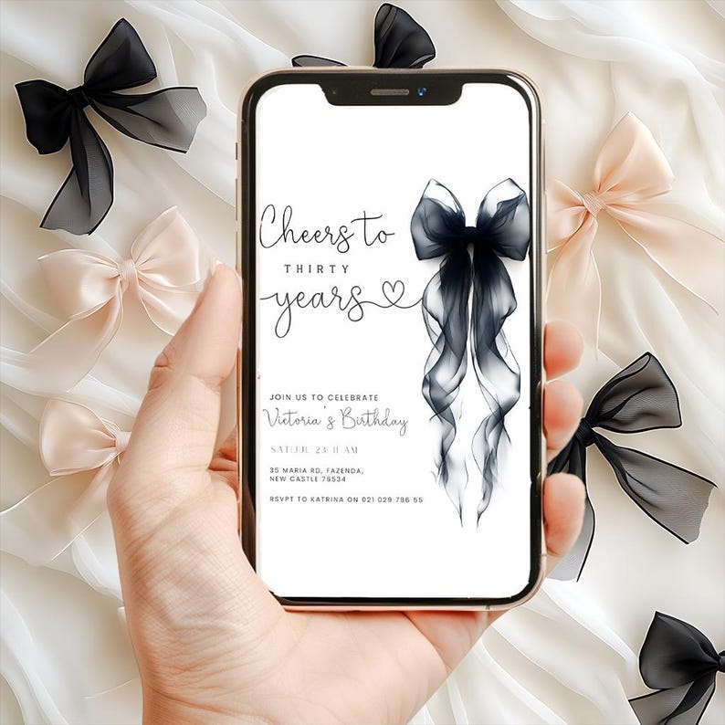 Może przedstawiać: Smartfon wyświetla zaproszenie urodzinowe z napisem "Cheers to Thirty Years". Zaproszenie zawiera ilustrację czarnej kokardy. Czarne i r&oacute;żowe kokardy są rozrzucone na białym tle materiału.