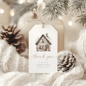 May include: A white gift tag with a watercolor illustration of a snow-covered house. The tag includes the words "thank you", the name "Love Jordana", and a date. The tag is tied with twine.