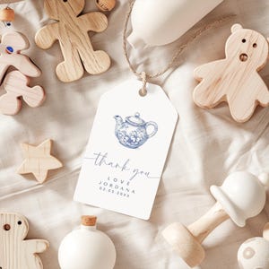 Peut inclure: Une &eacute;tiquette de remerciement blanche avec une illustration de th&eacute;i&egrave;re bleue et blanche. L'&eacute;tiquette dit "merci" en cursive et "love Jordana 02.03.20XX".