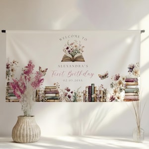 May include: A white banner with the text "WELCOME TO" above an open book illustration with flowers. Below, it reads "ALEXANDRA'S First Birthday 02.03.20XX". The banner features illustrations of books, flowers, and butterflies.
