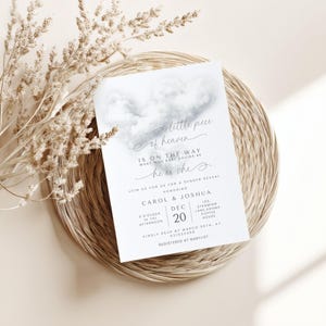 May include: A gender reveal invitation with the text "a little piece of heaven is on the way." The invitation features a watercolor cloud design and details for the event, including the date, time, and location.